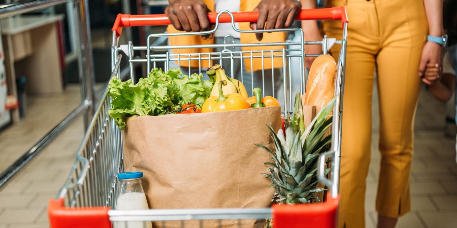 cropped image of young couple carrying shopping trolley with food in supermarket