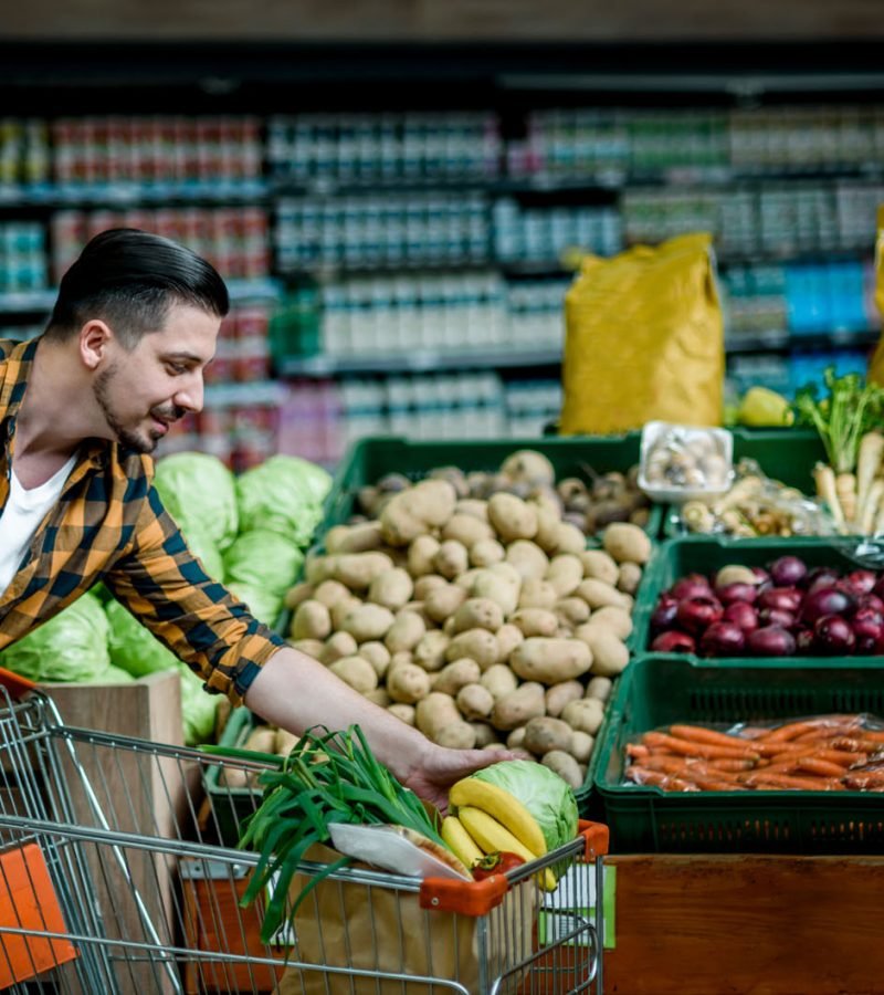 Young handsome man in a supermarket choosing products and holding shopping cart while grocery shopping